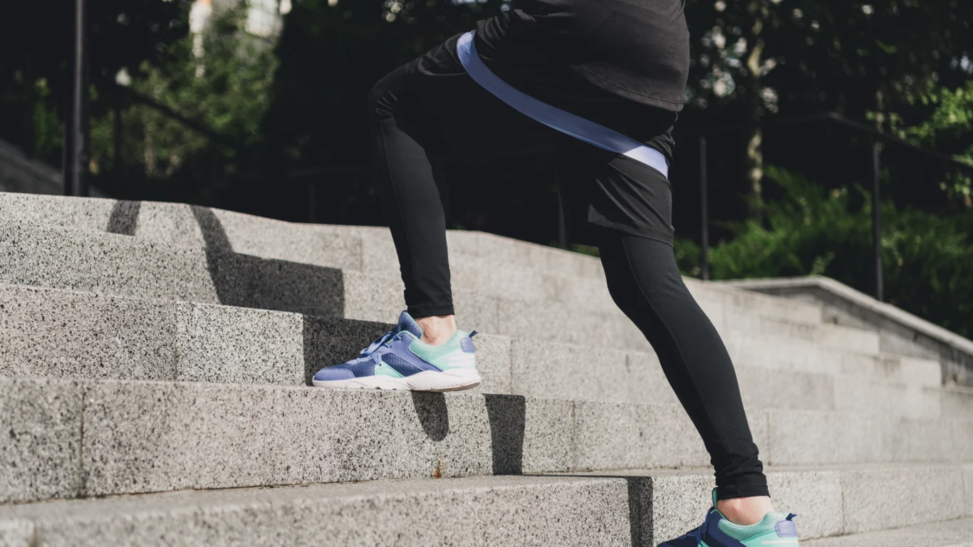 Person i träningskläder går uppför en bred stentrappa utomhus. Bilden fokuserar på ben och fötter i sportskor och symboliserar fysisk aktivitet, rörelse och vardagsträning. (Adobe)