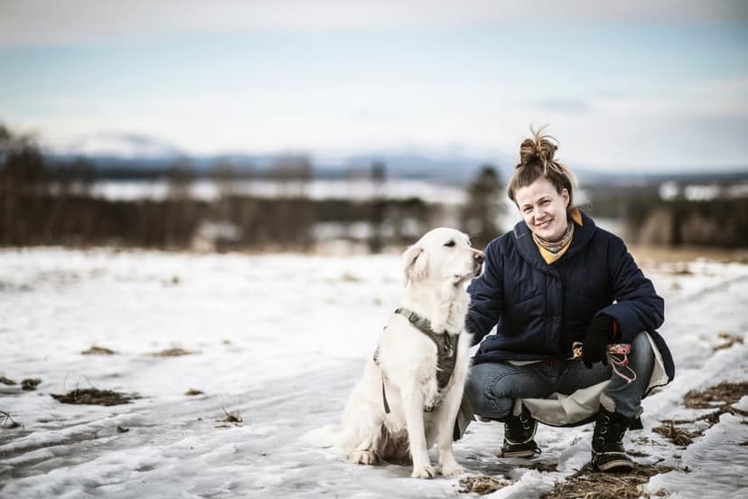 Lisa Ridzen ute med vita labradorhunden mot en bakgrund av snö. foto sandra lee pettersson