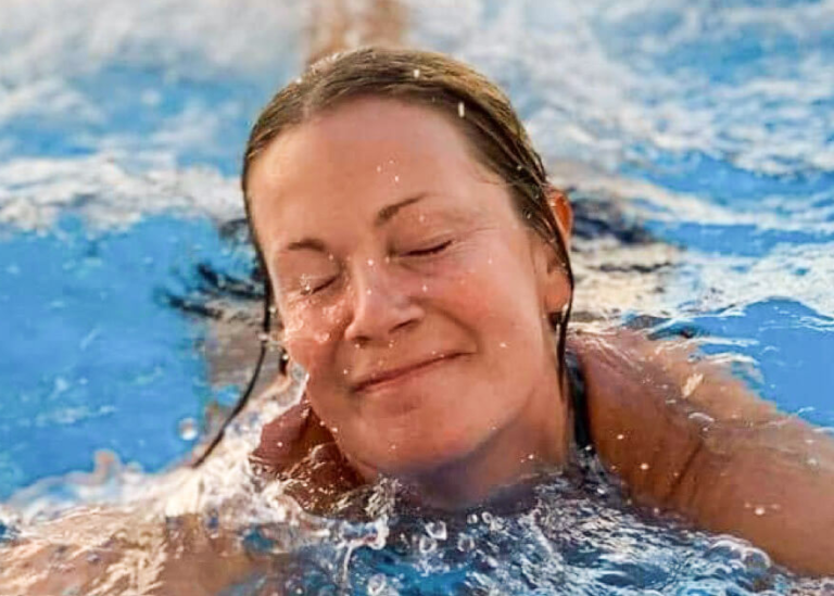 Kvinna som ler, blundar och  simmar i en bassäng.