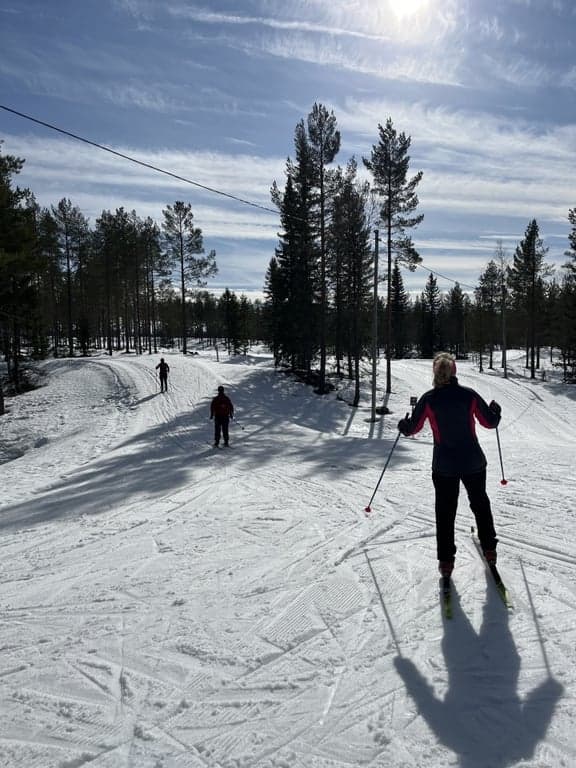 Vinterdag med längskidor, tre personer åker i ett längdskidspår i strålande sol. 